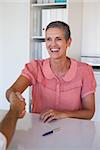 Laughing businesswoman shaking hands at desk in her office