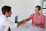 Casual business people shaking hands at desk in her office