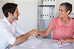 Casual business people shaking hands at desk and smiling in her office