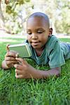 Little boy lying on grass looking at digital camera on a sunny day