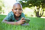 Little boy lying on grass holding digital camera smiling at camera on a sunny day