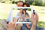 Hand holding tablet pc showing family sitting in the park