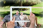 Hand holding tablet pc showing senior couple sitting on a bench