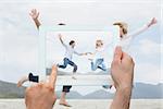 Hand holding tablet pc showing cheerful couple holding hands and jumping at beach