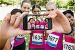 Hand holding smartphone showing confident female participants of breast cancer marathon