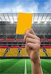 Hand holding up yellow card against stadium full of germany football fans
