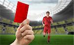 Hand holding up red card against football stadium and player