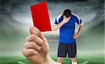 Composite image of hand holding up red card to player against football pitch in large stadium