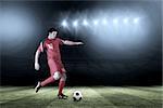 Football player in red kicking against football pitch under spotlights