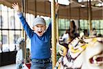 excited little boy enjoying his ride at carousel in amusement park