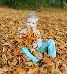 cute little boy sitting in colorful autumn leaves