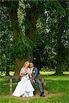beautiful young wedding couple in park, sitting on bench, blonde bride with flower and her groom