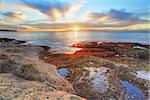 Beautiful red and green covered rocks light up as they catch the first rays of morning sunshine at South Coogee, Eastern suburb of Sydney, Australia taken just after sunrise.