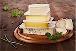 Luxurious cheese variation on wooden board with parsley and chive.