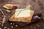 Cheese on wooden board with bread, onion piece, chive and wheat. Natural agricultural vintage style concept.