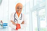 Cheerful young Muslim female doctor portrait, standing inside hospital