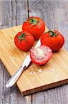 Ripe Tomatoes Full Body and Halves with Salt Flakes and Table Knife on Wooden Cutting Board