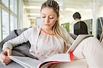 Young businesswoman with digital tablet reading book in office