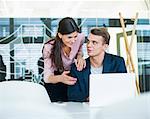Young businessman with female colleague discussing over laptop at table in office
