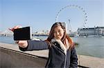 Portrait woman taking self portrait through cell phone against London Eye at London, England, UK