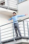Full length of smiling young businessman standing arms outstretched at hotel balcony