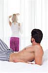 Shirtless man looking at woman standing by window in hotel room