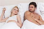 Angry young couple looking at each other in bed