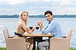 Side view portrait of young couple holding hands at outdoor restaurant by lake