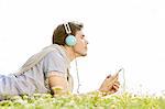 Side view of man enjoying music on MP3 player using headphones in park against clear sky