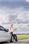 Full length of mid adult woman leaning on car while reading map at countryside