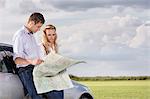 Couple reading map while leaning on car at countryside