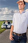 Young man shielding eyes with woman and car in background at countryside