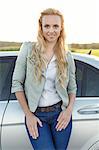Portrait of attractive young woman standing by car at countryside