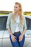 Beautiful young woman looking away while standing by car at countryside