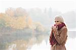 Thoughtful young woman wearing muffler at lakeside in park