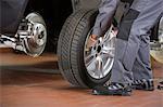 Low section of repairman fixing car's tire in repair shop