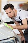 Young maintenance engineer cleaning car in repair shop