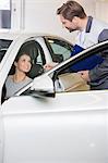 Automobile mechanic giving car key to female customer in repair shop