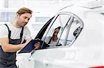 Automobile mechanic writing on clipboard while examining car in repair shop