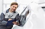 Portrait of confident automobile mechanic holding clipboard while leaning on car's window in workshop