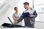 Young male engineer explaining car engine to female customer in workshop