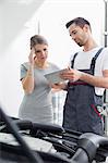 Male maintenance engineer showing digital tablet to worried customer at workshop