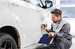 Male repair worker examining car paint with equipment in repair shop