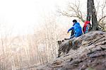 Side view of male hiker sitting on edge of cliff in forest