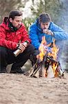 Male backpackers having coffee at campfire in forest