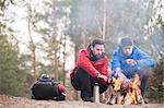 Male hikers warming hands at campfire in forest