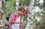 Backpacker reading map while leaning on tree trunk in forest