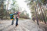 Rear view of hiking couple holding hands while walking in forest