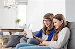 Happy sisters using digital tablet on sofa at home