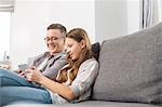 Father and daughter using digital tablet on sofa at home